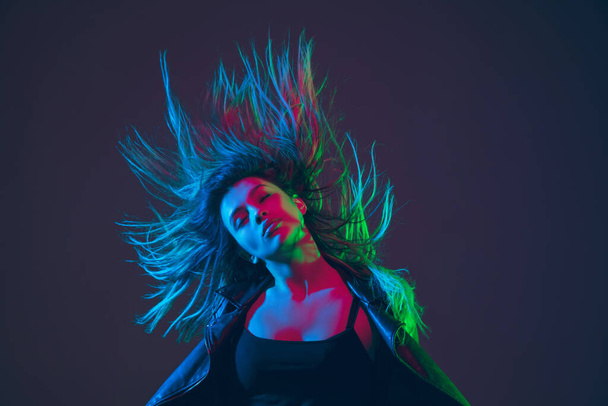 Beautiful womans portrait with blowing hair on dark studio background in colorful neon light - Fotó, kép