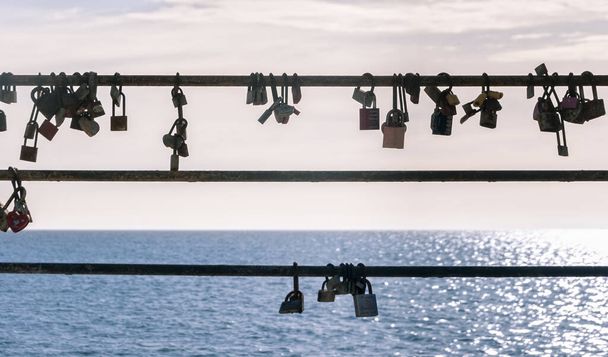 Fechaduras de amantes contra a luz em um corrimão de metal de frente para o Mar Mediterrâneo sem foco. Promenade de Cala Millor, ilha de Maiorca, Espanha
 - Foto, Imagem