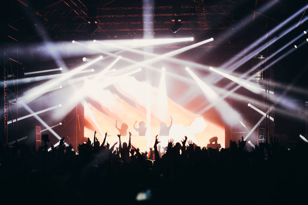 Bühnenbeleuchtung und Publikum mit erhobenen Händen bei einem Musikfestival. Fans genießen die Party-Stimmung. - Foto, Bild