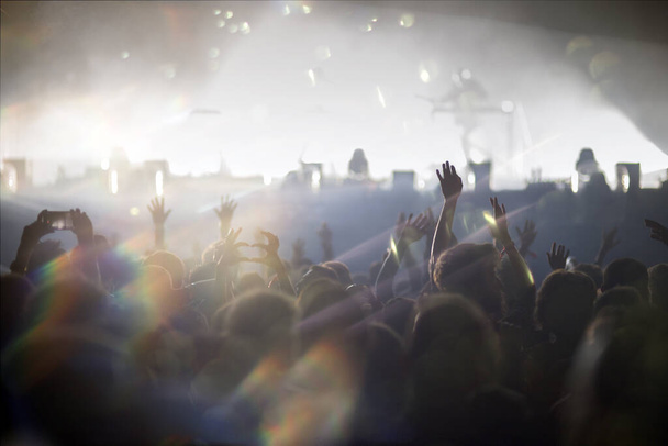 Stage lights and crowd of audience with hands raised at a music festival. Fans enjoying the party vibes. - Photo, Image