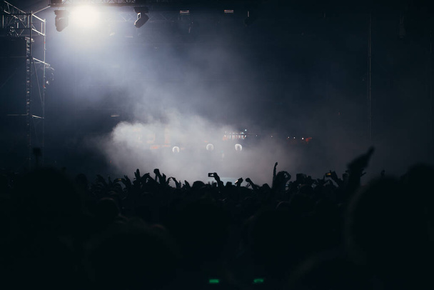 Sahne ışıkları ve bir müzik festivalinde elleri havada seyirci kalabalığı. Taraftarlar parti havasını seviyor. - Fotoğraf, Görsel