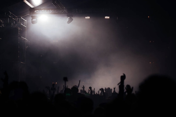 Sahne ışıkları ve bir müzik festivalinde elleri havada seyirci kalabalığı. Taraftarlar parti havasını seviyor. - Fotoğraf, Görsel