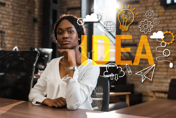 attractive, thoughtful african american businesswoman sitting at desk and looking at camera, idea illustration - Foto, Imagen