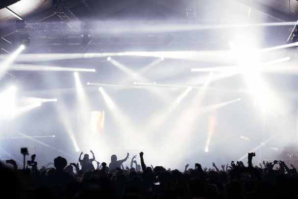 Podiumlichten en publiek met opgeheven handen op een muziekfestival. Fans genieten van de feestvibes. - Foto, afbeelding