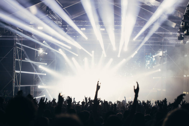 Luzes de palco e multidão de público com as mãos levantadas em um festival de música. Fãs curtindo as vibrações de festa
. - Foto, Imagem