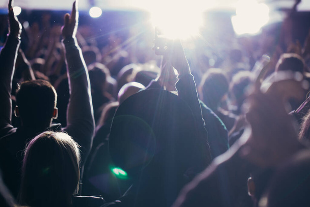 Színpadi fények és közönségtömeg felemelt kézzel egy zenei fesztiválon. Rajongók élvezik a party vibrálást. - Fotó, kép
