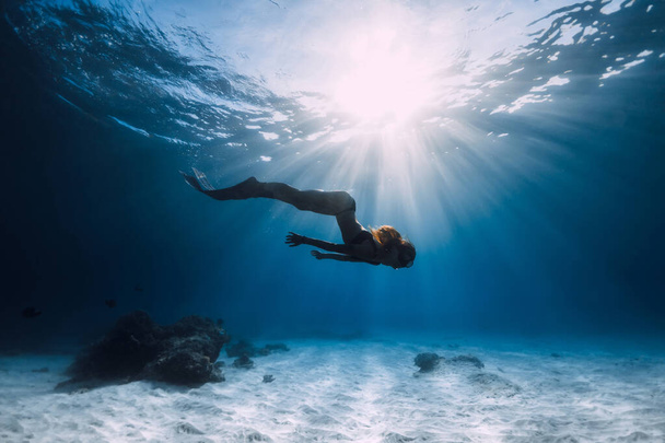 女性のフリーダイバーは、砂の海の底の上にフィンで滑ります。青い海のフリーダイビングと太陽の光 - 写真・画像