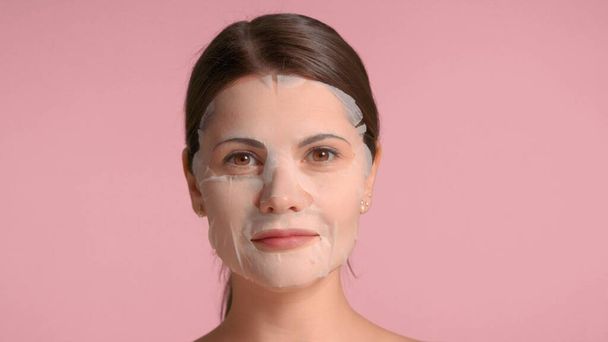 30代のブルネットの女性のクローズアップ肖像画シートマスクを示しています。セルフケアの概念 - 写真・画像