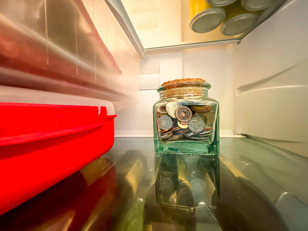 Glasgefäß mit Geld aus verschiedenen Ländern am Boden des Kühlschranks - Foto, Bild