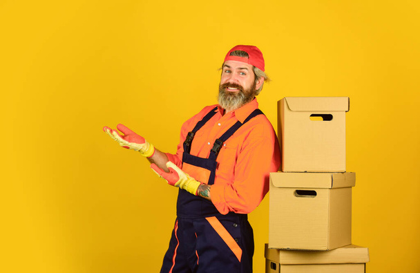 Successful engineer. move to new apartment. bearded loader in uniform. Cardboard boxes. moving to new house. purchase of new habitation or repair of room. Man wearing boilersuit packing boxes - Foto, afbeelding