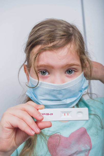 Worldwide coronavirus epidemic concept. Pandemic COVID-19, 2019-nCoV. Kid girl with positive test strip for antibody or sars-cov-2 virus disease in hands. White background - Foto, Imagem