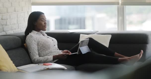 Portrait of black woman doing meeting or web conference from home. African american people doing remote work. Young businesswoman working with laptop computer, lying on sofa - Materiaali, video