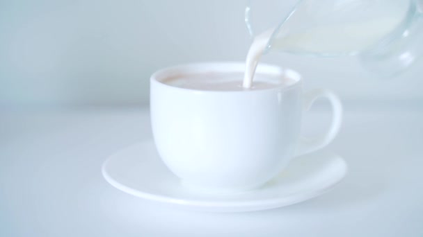 pour the cream or milk into the coffee into a white cup. white background. light table. morning coffee. side view - 映像、動画
