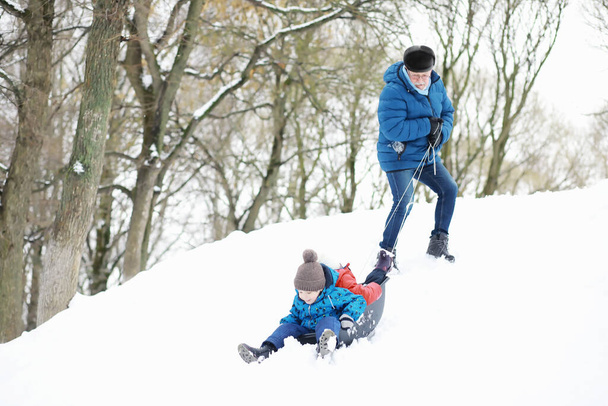 Niños en el parque en invierno. Los niños juegan con nieve en el patio. Esculpen muñecos de nieve y se deslizan por las colinas. - Foto, imagen