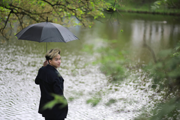 Весенний парк в дождливую погоду и молодой человек с амбреллом
 - Фото, изображение