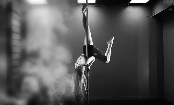 Girl doing exercises on a sports equipment. The dancer on the pylon in the studio. - Photo, image