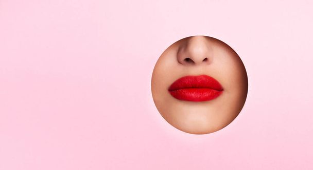 Woman showing red lips in pink paper hole - Фото, зображення