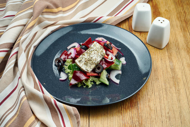 Classic Greek salad with tomatoes, onions, cucumber, feta cheese and black olives in black plate on a wooden background. Close up view. Food flat lay - Foto, Imagem