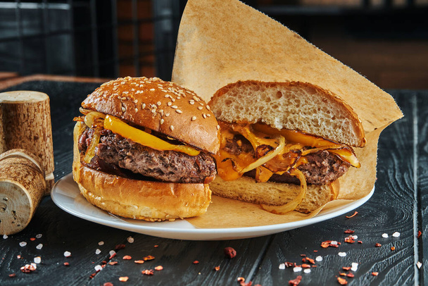 Appetitlich und saftig halbgeschnittener Burger mit einem großen Rindfleischpatty, Zwiebeln und Paprika auf einem weißen Teller mit Pommes frites. Nahaufnahme - Foto, Bild