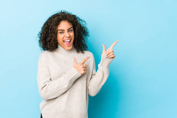 Joven africana americana cabello rizado mujer señalando con los dedos índice a un espacio de copia, expresando emoción y deseo
. - Foto, Imagen