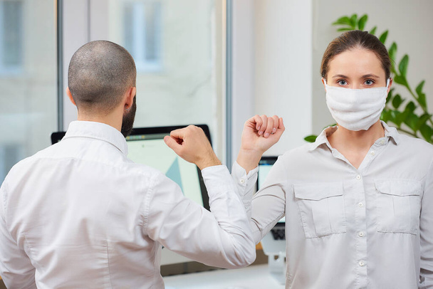 Saludo del codo para evitar la propagación del coronavirus (2019-nCoV). La mujer con una mascarilla médica y el hombre se encuentran en una oficina con las manos desnudas. En lugar de saludar con un abrazo o un apretón de manos, golpean los codos
 - Foto, imagen