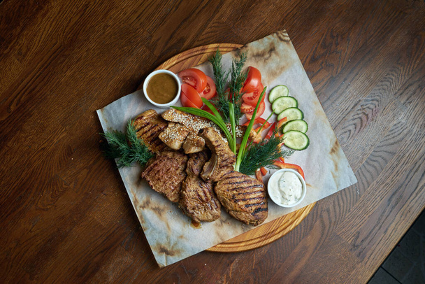 A large portion of grilled kebab. Pork fillet, steak on the bone cooked in a barbecue with different sauces and fresh vegetables. Shashlic. Top view food meat. - Photo, image