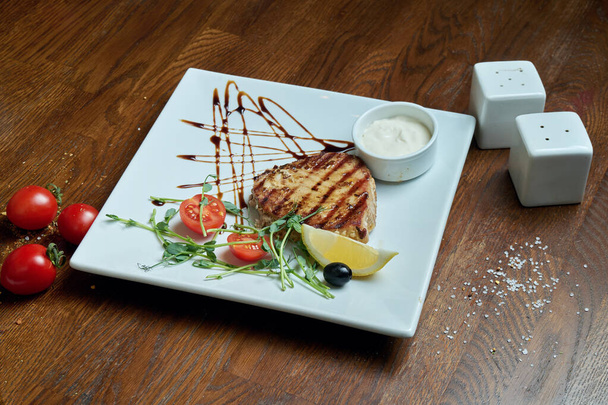 Close up view on tasty and juicy tuna steak in plate in a composition with spices on a wooden background - Foto, imagen