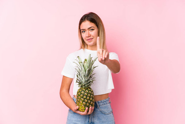 jonge blanke vrouw met een ananas waarop nummer een met vinger. - Foto, afbeelding