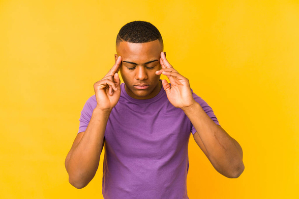 Junger lateinischer Mann auf gelbem Hintergrund isoliert, berührt Schläfen und hat Kopfschmerzen. - Foto, Bild