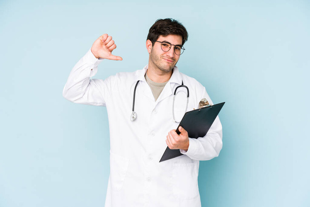 Young doctor man isolated on blue background feels proud and self confident, example to follow. - Foto, imagen