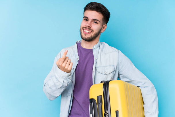 Junger kaukasischer Reisender, der isoliert einen Koffer hält und mit dem Finger auf dich zeigt, als ob er dich einladen würde, näher zu kommen. - Foto, Bild