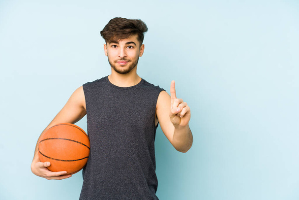 Νεαρός άνδρας από την Αραβία παίζει μπάσκετ απομονωμένος δείχνοντας νούμερο ένα με το δάχτυλο. - Φωτογραφία, εικόνα