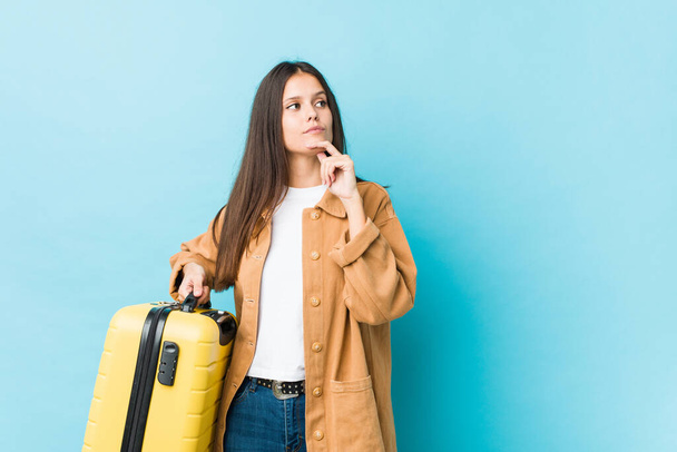 Молода біла жінка тримає валізу, дивлячись вбік з сумнівним і скептичним виразом
. - Фото, зображення