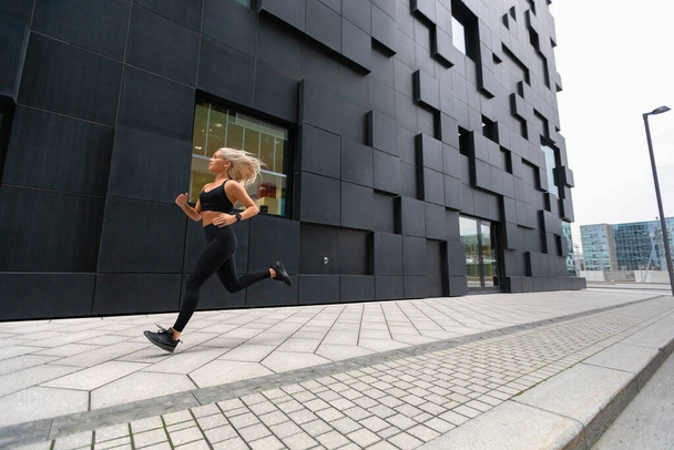 Nopea käynnissä oleva nainen yllään urheilu alkuun modernissa kaupunkiympäristössä
 - Valokuva, kuva
