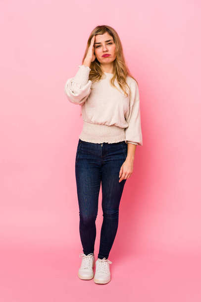 Young blonde caucasian woman standing over a pink background tired and very sleepy keeping hand on head. - Фото, зображення