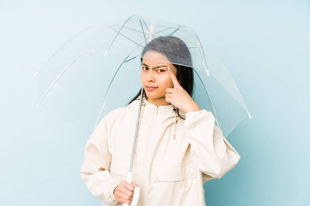 Jeune femme chinoise tenant un parapluie isolé pointant du doigt vers vous comme si vous invitant se rapprocher
. - Photo, image