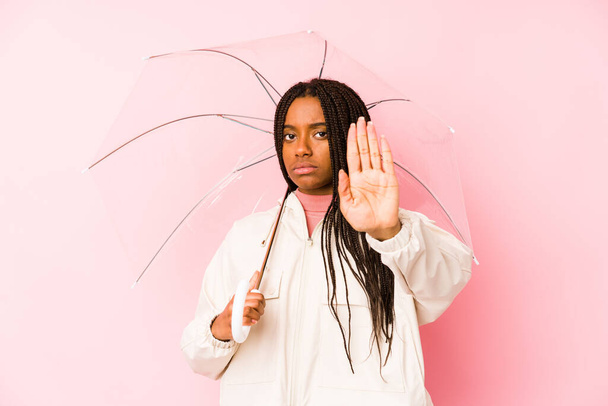 Молода афроамериканська жінка, що тримає парасольку ізольованою стоячи з розтягнутою рукою, показує знак "Стоп", запобігаючи вам. - Фото, зображення