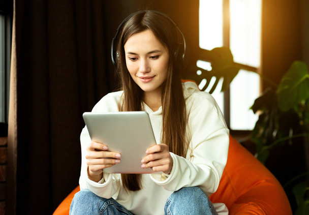 Modern girl with tablet and headphones works in bag chair - Photo, Image
