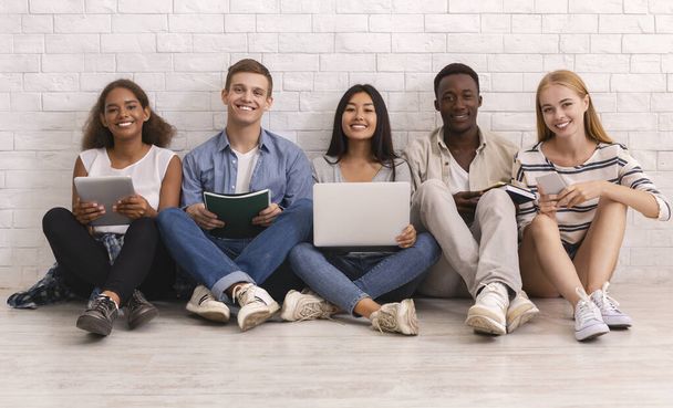 Χαμογελαστή ομάδα διεθνών φοιτητών που μελετούν πάνω από λευκό τοίχο τούβλο - Φωτογραφία, εικόνα