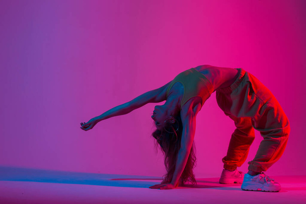 Sportowa młoda kobieta w stroju sportowym robi ćwiczenia jogi w pokoju w kolorze czerwonym w stylu disco. Dziewczyna instruktor jogi robi fitness w studio z niesamowitym multi-kolorowe światło. - Zdjęcie, obraz