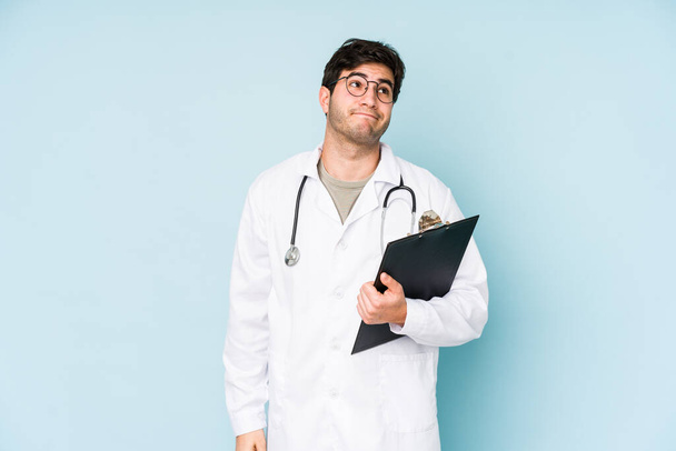 Young doctor man isolated on blue background dreaming of achieving goals and purposes - Photo, Image