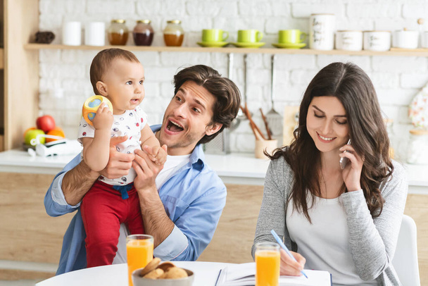 Cheerful daddy playing with baby son, his wife consulting partners by phone - Photo, Image