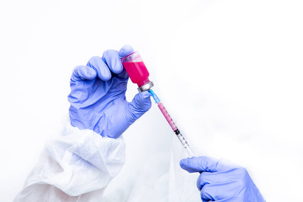 Hands of a virologist in a virus-proof suit and medical gloves fills a syringe with medicine. hands with a syringe on a white background. - Foto, imagen