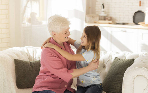 Pequena criança e sua avó abraçando uns aos outros no sofá
 - Foto, Imagem