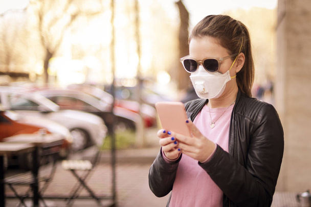 Shot of young woman wearing a respirator mask device for health protection and text messaging while walking on the street. Confident woman wearing face mask while rapidly spreading coronavirus outbreak. - Φωτογραφία, εικόνα