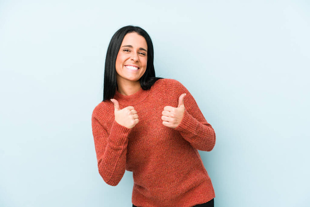 Молодая белая женщина, изолированная на синем фоне, поднимает оба больших пальца вверх, улыбаясь и уверенно
. - Фото, изображение