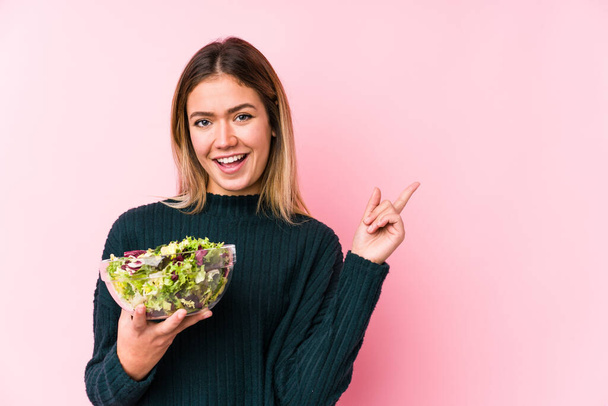 Молодая белая женщина держит салат изолированный улыбаясь весело указывая указательным пальцем
. - Фото, изображение