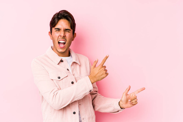 Joven hombre caucásico posando en un fondo rosa aislado señalando con los dedos índice a un espacio de copia, expresando emoción y deseo
. - Foto, Imagen