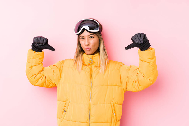 Nuori valkoihoinen nainen yllään hiihtovaatteet vaaleanpunainen tausta tuntuu ylpeä ja itsevarma, esimerkki seurata
. - Valokuva, kuva