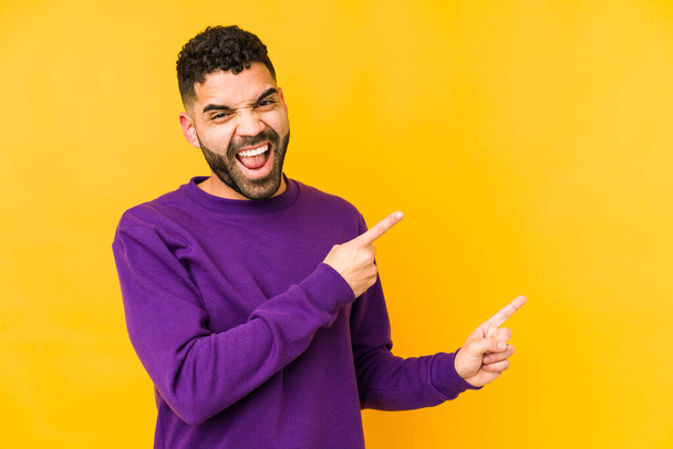 Junger arabischer Mann mit gemischter Rasse zeigt isoliert mit den Zeigefingern auf einen Kopierraum und drückt damit Begeisterung und Wunsch aus. - Foto, Bild
